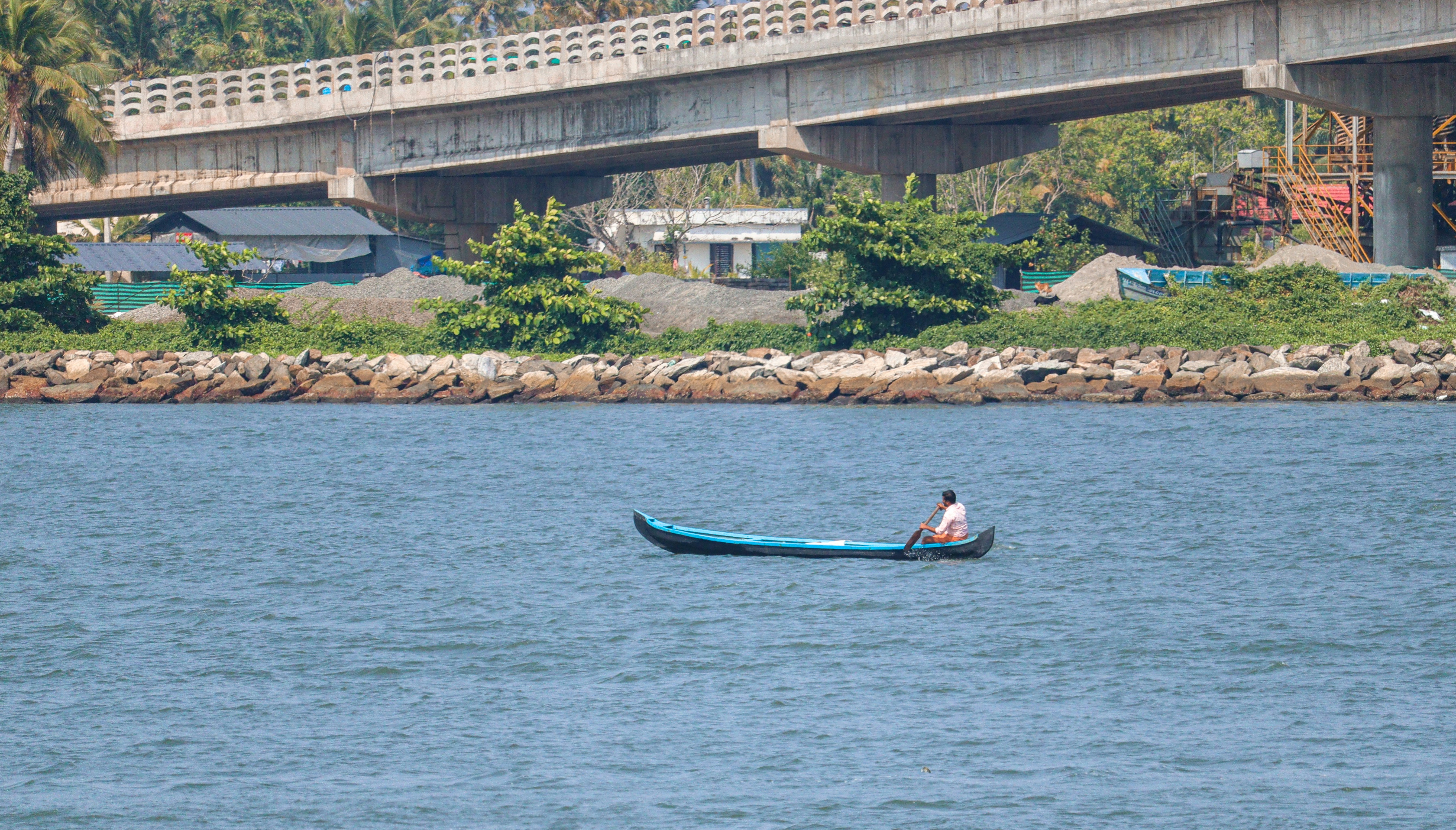 man riding on blue kayak on blue sea near bridge during daytime