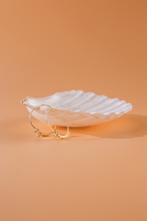 A pair of gold hoop earrings with subtle engraved details on a soft beige background.