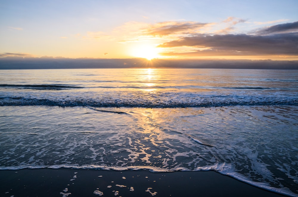 ocean waves crashing on shore during sunset