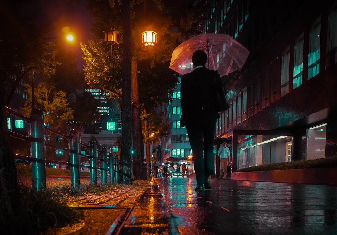 person in black jacket holding umbrella walking on sidewalk during night time