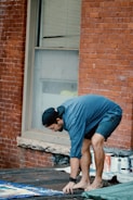 man in blue t-shirt and blue denim jeans sitting on brown concrete brick wall during
