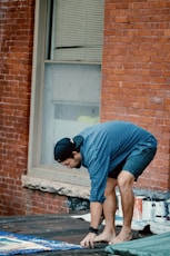 man in blue t-shirt and blue denim jeans sitting on brown concrete brick wall during