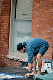 man in blue t-shirt and blue denim jeans sitting on brown concrete brick wall during