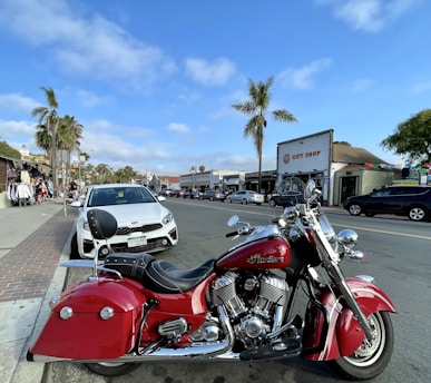 A vibrant red motorcycle parked near a colorful street market in Panjim under clear blue skies.