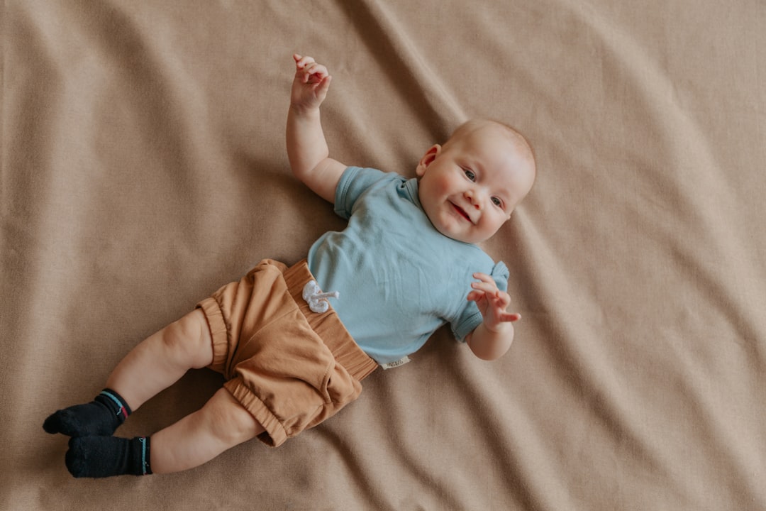 baby in blue shirt and orange pants lying on brown textile