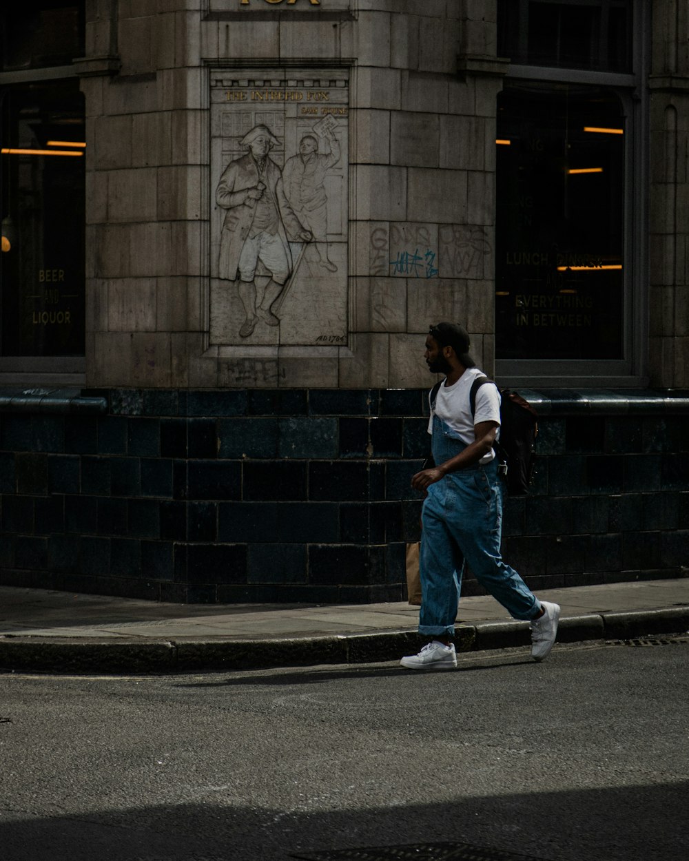 man in white t-shirt and blue denim jeans walking on sidewalk during daytime