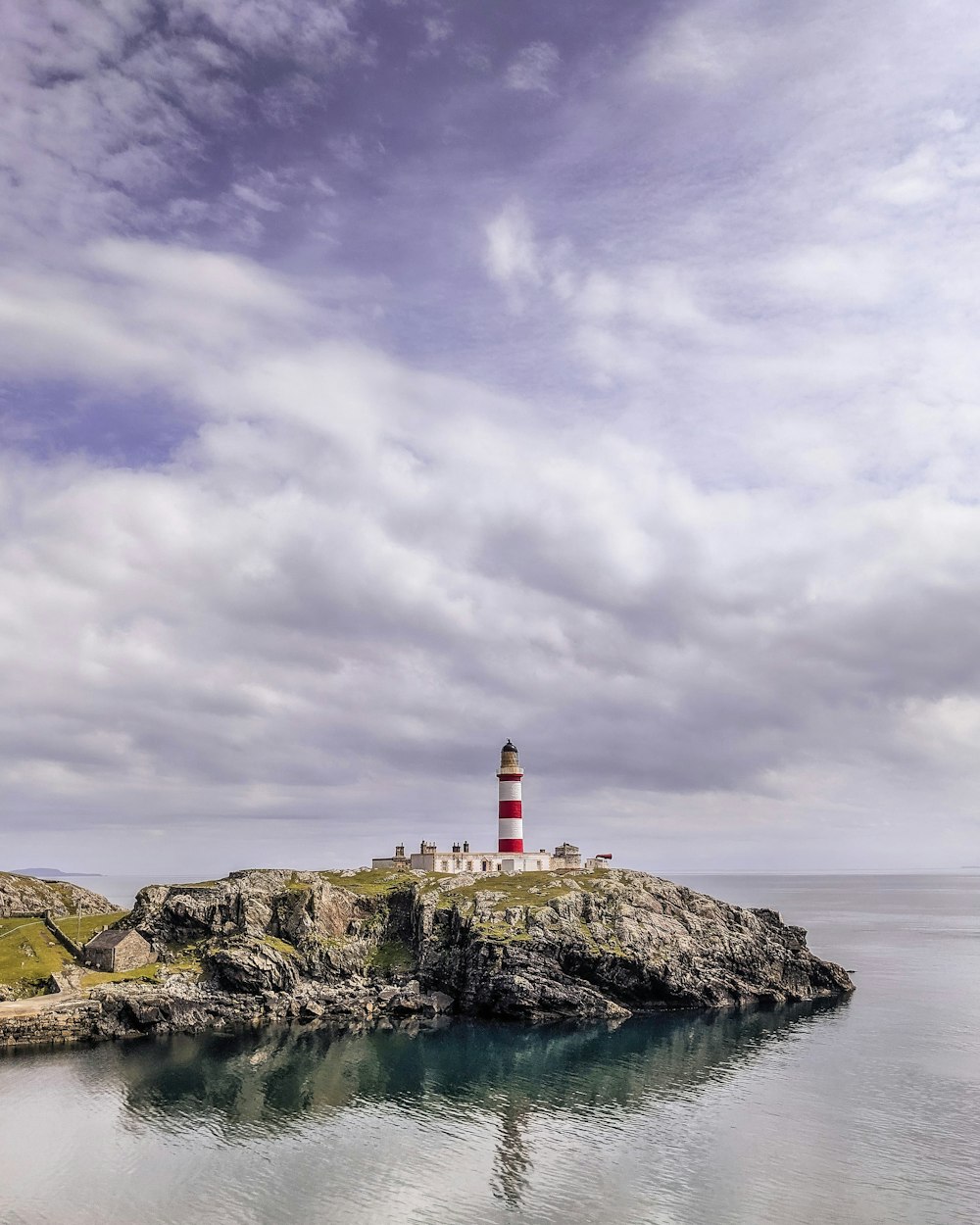 white and red lighthouse on brown rock formation near body of water under cloudy sky during