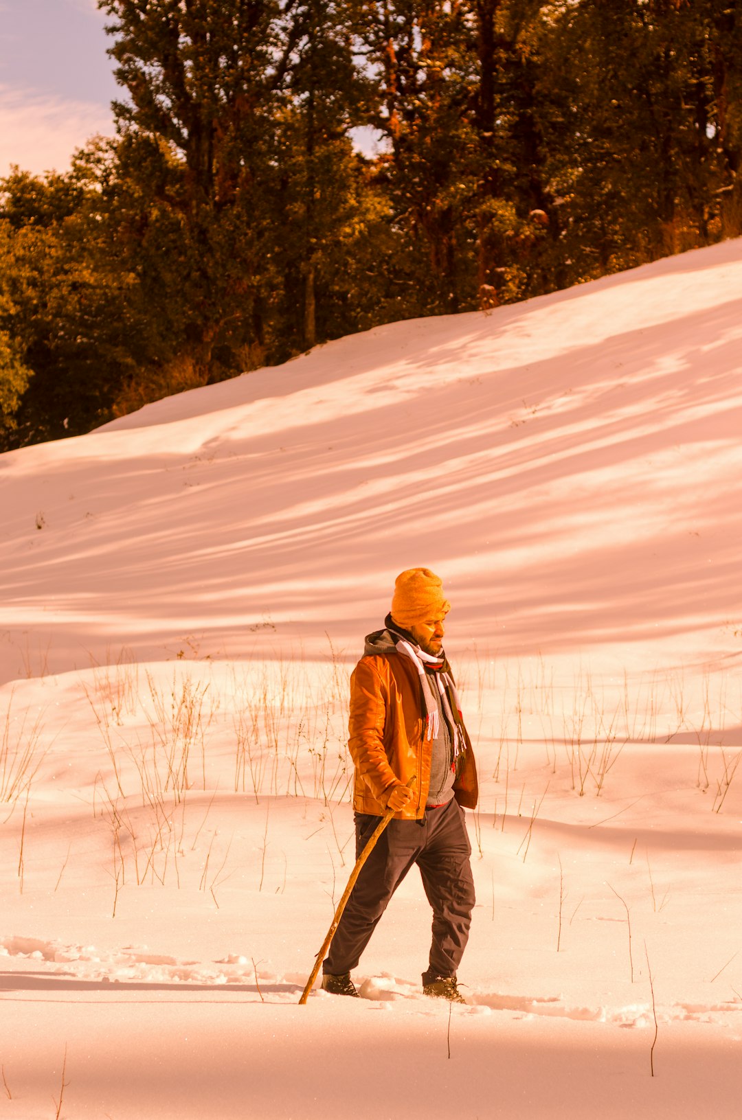 woman in brown jacket and black pants walking on snow covered field during daytime