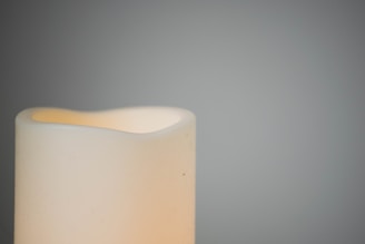 A softly lit candle on a cream-colored table with golden accents in the background