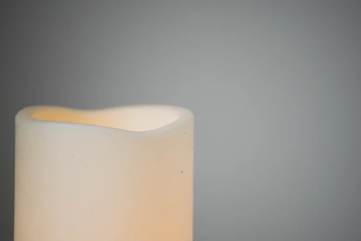A serene flat lay of a cream-colored journal, a gold pen, and a softly glowing candle on a minimalist white desk.