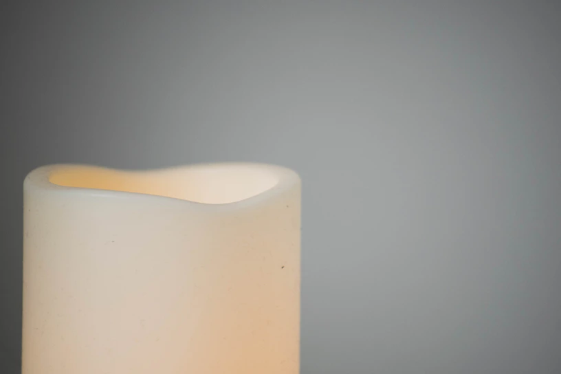 A cozy, minimalist black and white photo of a soy candle with natural frosting texture glowing softly on a wooden table.