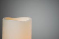 A soft-lit, partially visible cream-colored candle against a muted gray background, creating a serene and minimalist composition.