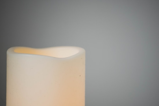 A soft-lit, partially visible cream-colored candle against a muted gray background, creating a serene and minimalist composition.