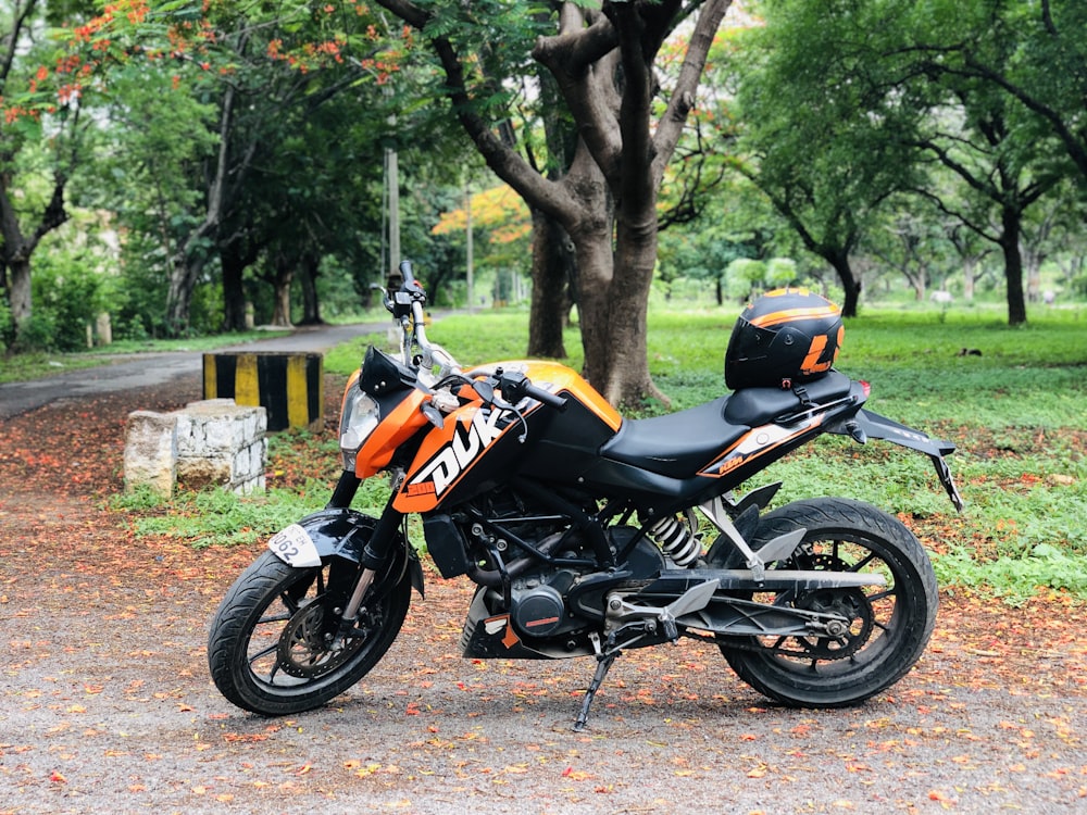 orange and black sports bike parked on dirt road near trees during daytime