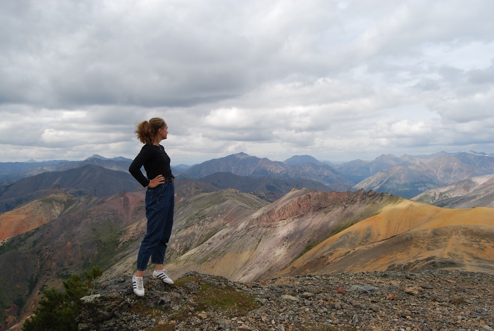 mulher na jaqueta preta de pé no solo rochoso olhando para as montanhas durante o dia