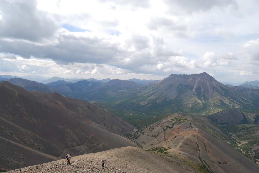 Persone che camminano sul campo marrone vicino alle montagne verdi sotto le nuvole bianche durante il giorno