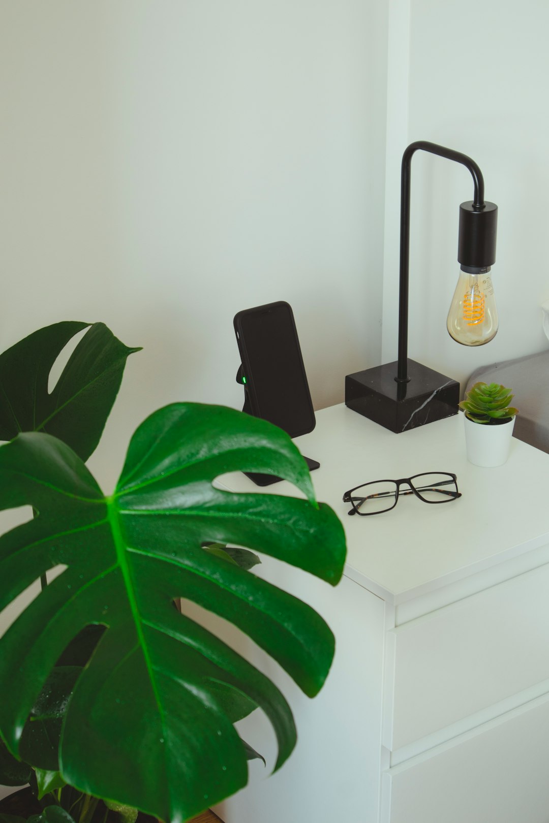black framed eyeglasses beside black smartphone and green plant