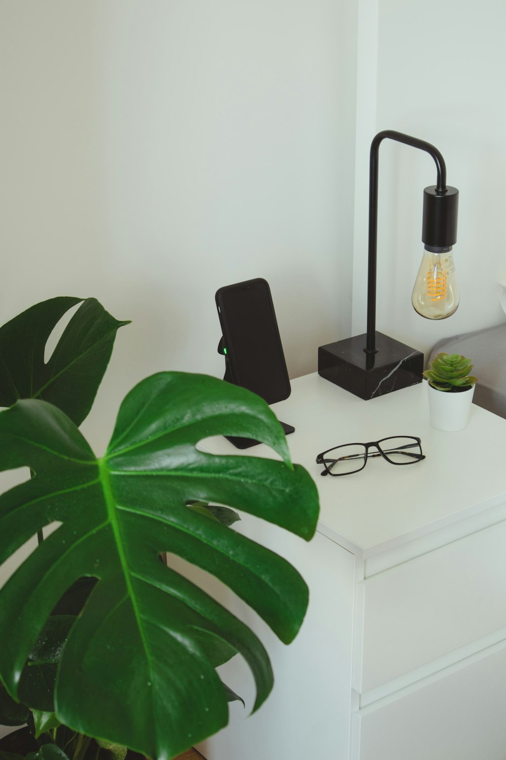 gafas con montura negra junto a un smartphone negro y una planta verde