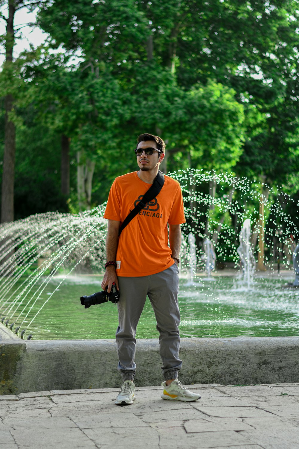 man in orange and black nike crew neck t-shirt and white pants standing near water