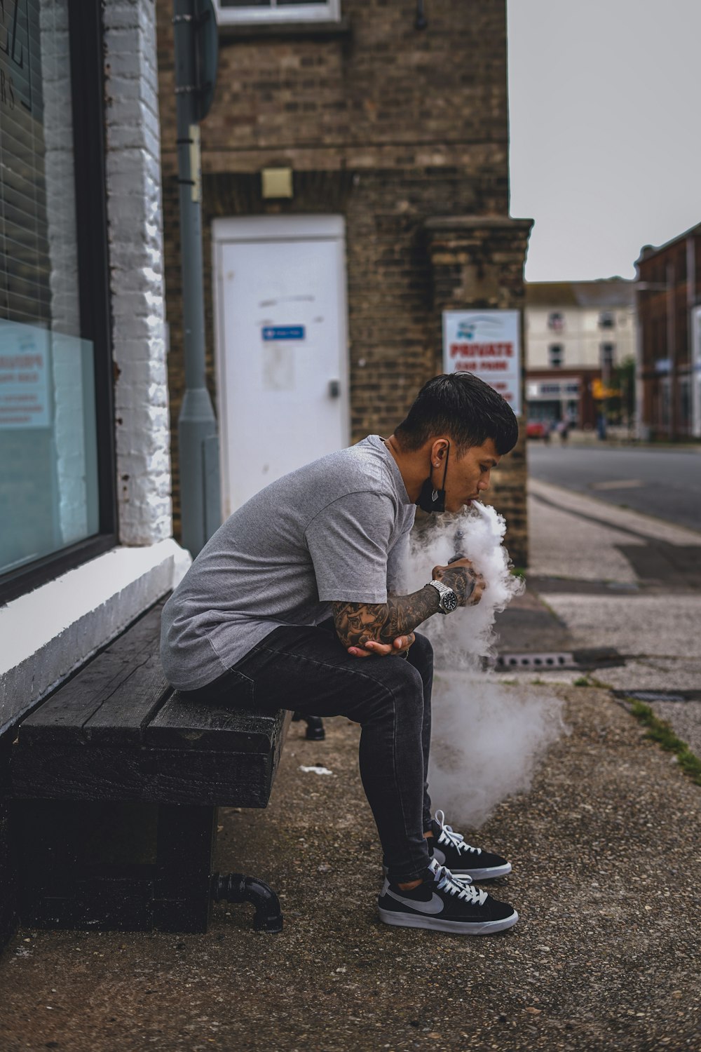 man in gray sweater smoking cigarette sitting on bench during daytime