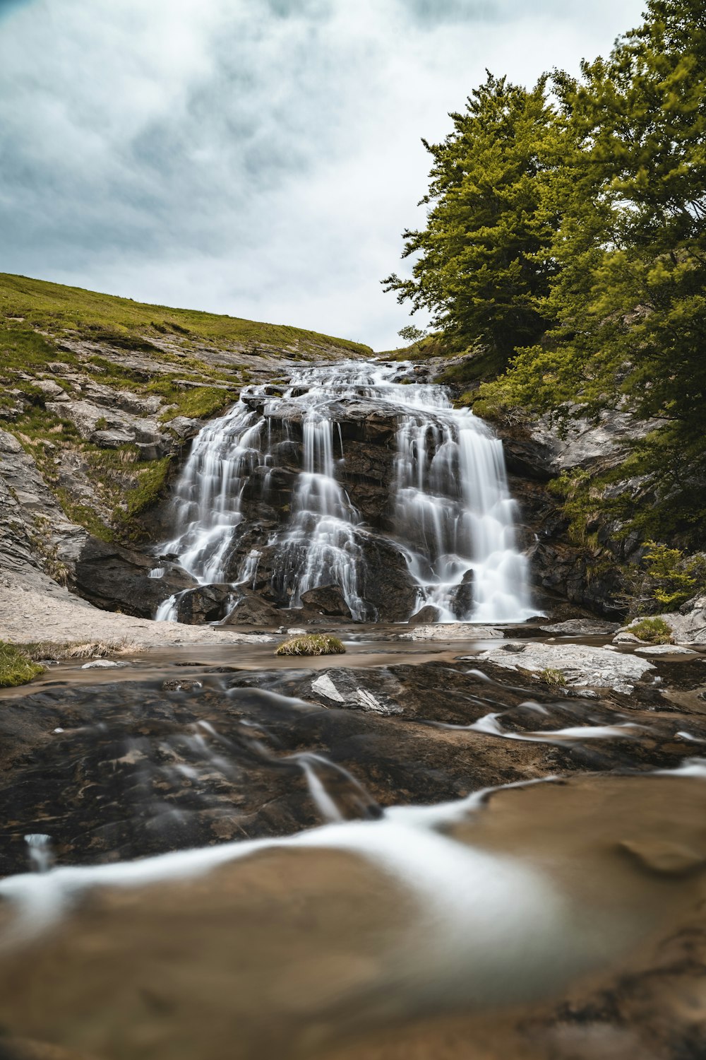 waterfalls on brown rocky mountain under gray cloudy sky