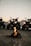 A group of all-terrain vehicles (ATVs) parked on a dirt surface with a small campfire in front. The background features a mountainous landscape under a twilight sky, adding a sense of adventure to the scene. The headlights of the ATVs are on, casting light towards the viewer.