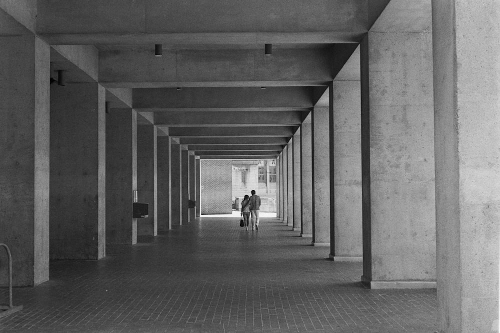 grayscale photo of 2 people walking on hallway