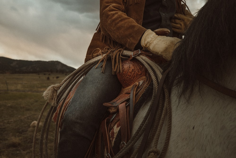 Femme en veste en cuir marron chevauchant un cheval blanc pendant la journée