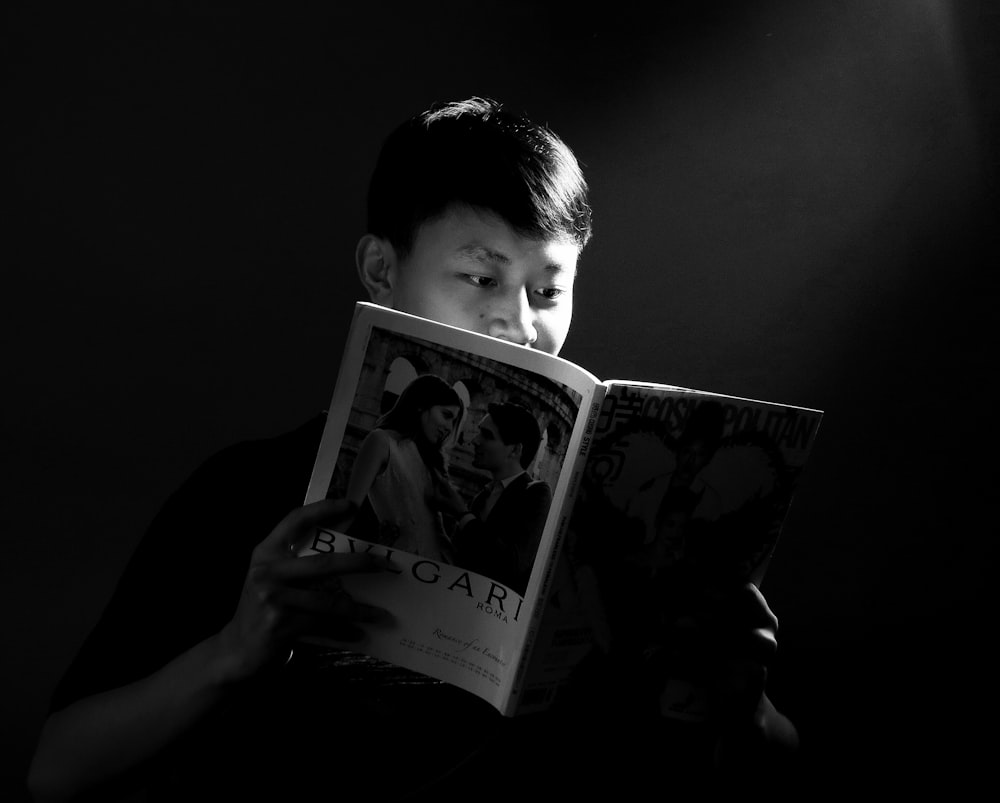 grayscale photo of boy holding book