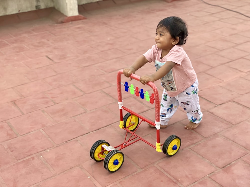 fille en robe à fleurs blanche et rose chevauchant un tricycle rouge et jaune