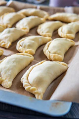 Hands arranging empanadas on rustic bakery display shelves.