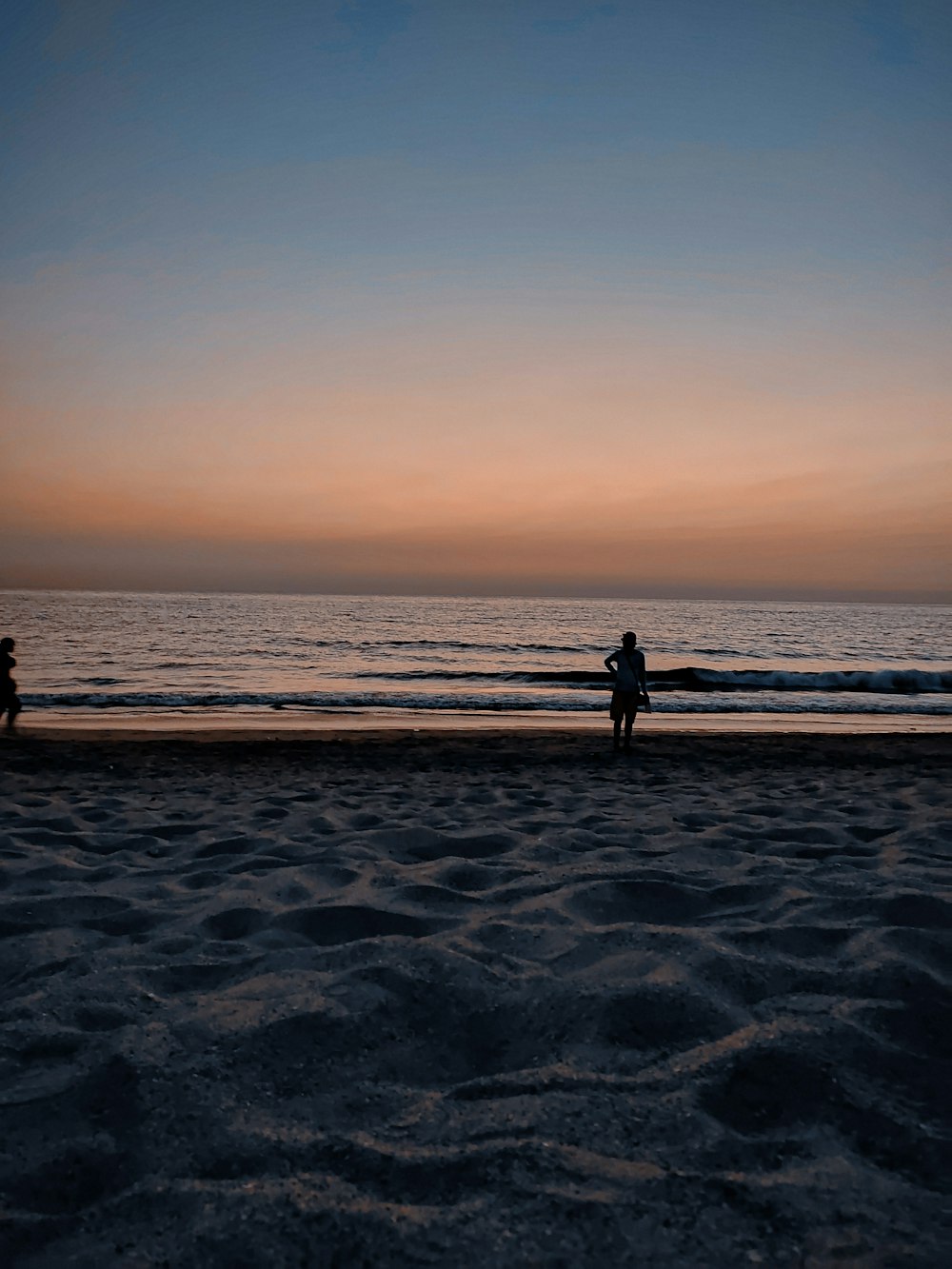 silhouette of 2 people standing on beach during sunset