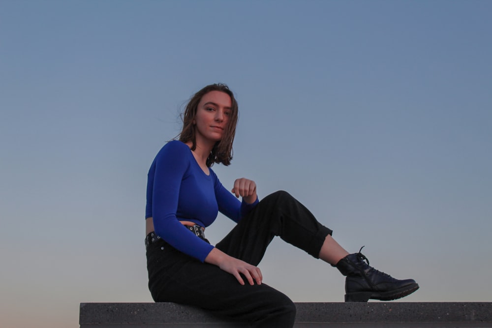 woman in blue long sleeve shirt and black pants sitting on concrete bench during daytime