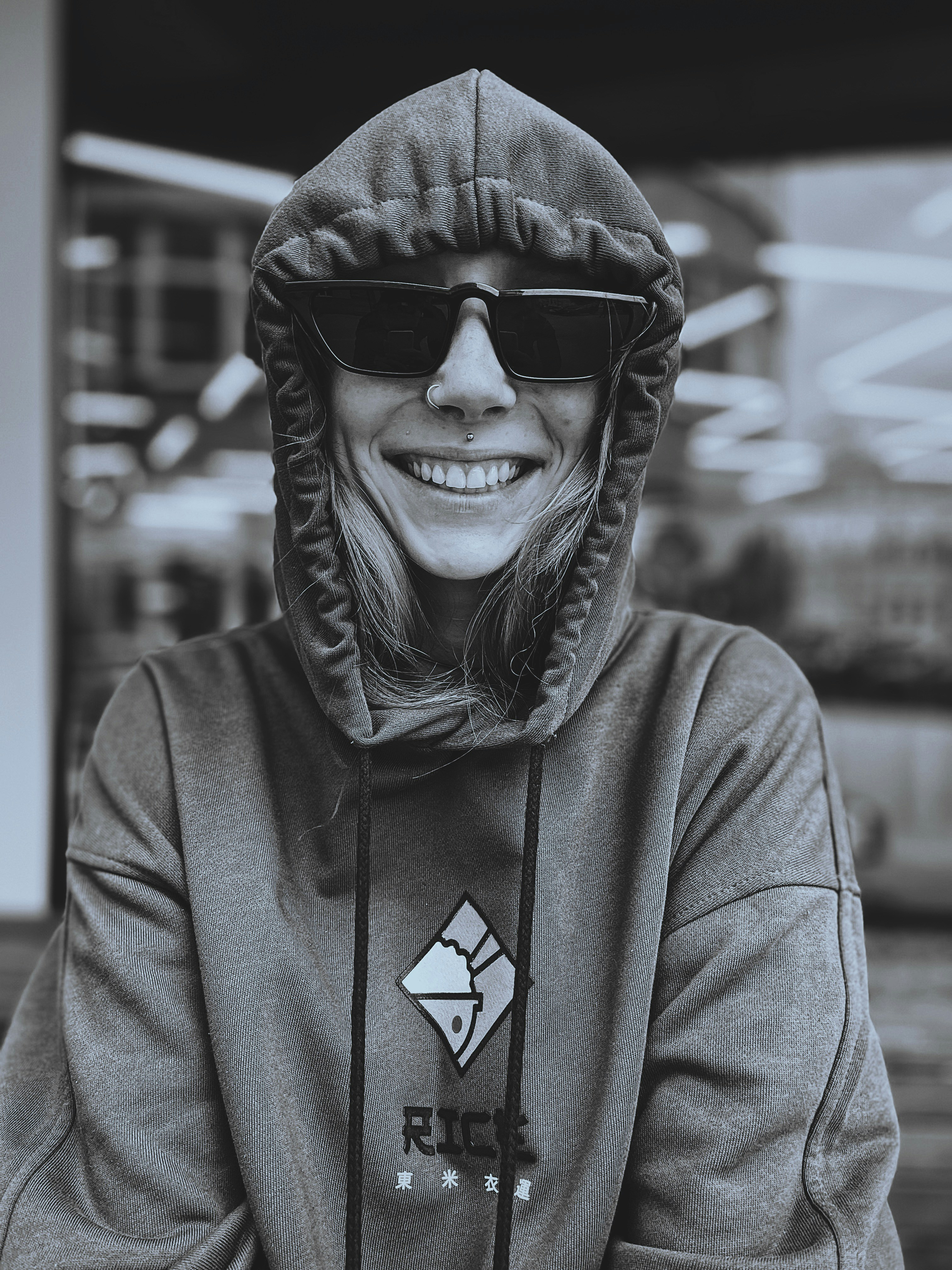 Close-up of a customer smiling while wearing a sleek black elevencol hoodie in a bright urban setting.