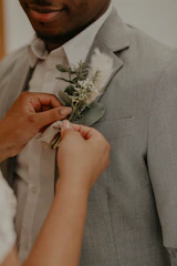 A groom adjusting his tie in a softly lit room with black and white tones and a yellow boutonniere.