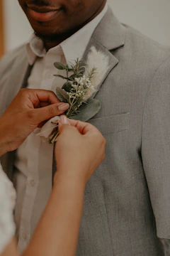 A groom adjusting his tie in a softly lit room with black and white tones and a yellow boutonniere.
