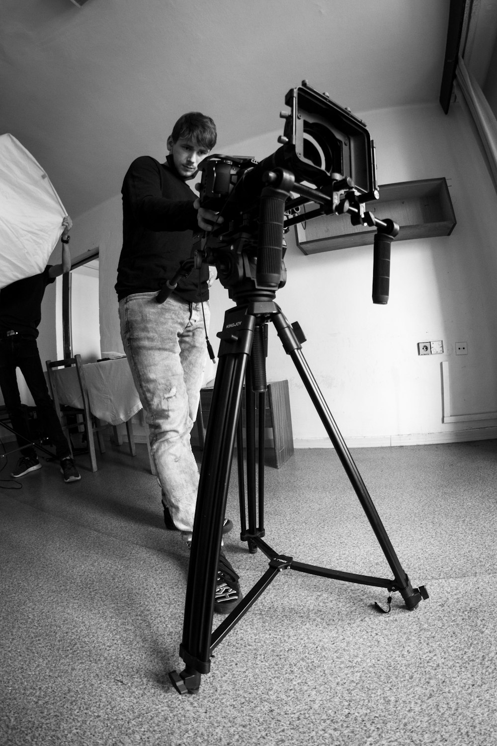 man in black jacket and pants standing in front of camera with tripod