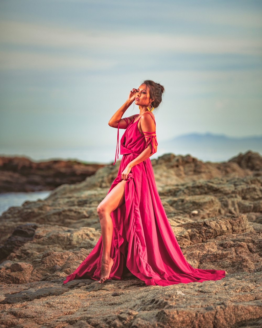 woman in pink dress standing on brown sand near body of water during daytime