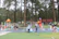 Parents watching happily as their kids play on a large green and beige inflatable slide in a forest setting.