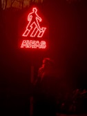 A glowing red warning sign with the word 'AWAS' and an outline of a person descending steps. Below the sign, a person is partially visible, standing in the dark and holding something near their face.
