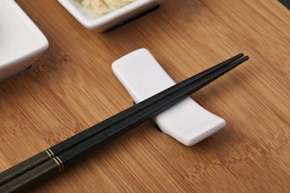 A pair of polished chopsticks resting on a minimalist ceramic holder beside a lunch box.