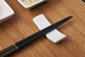 A pair of polished chopsticks resting on a minimalist ceramic holder beside a lunch box.