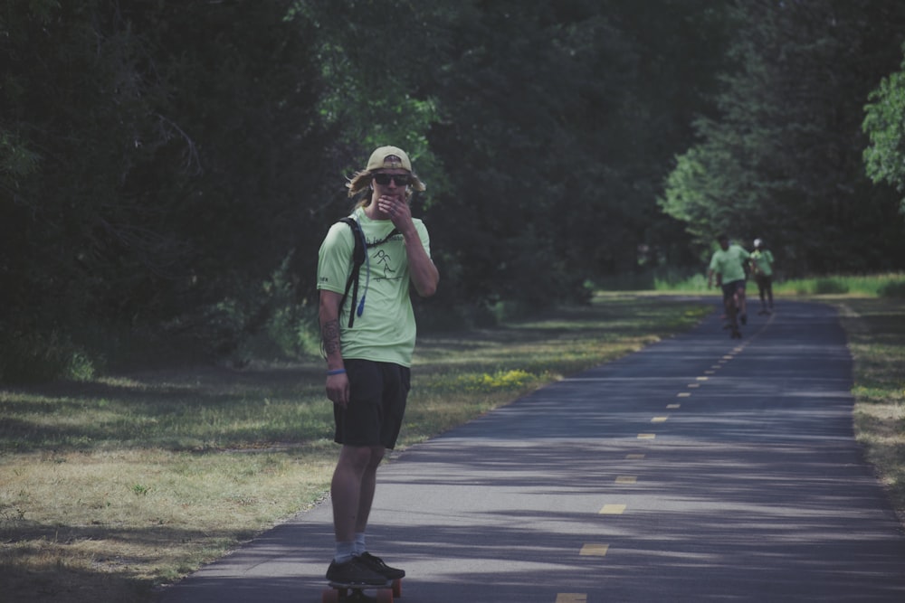 woman in green shirt and black shorts walking on gray asphalt road during daytime