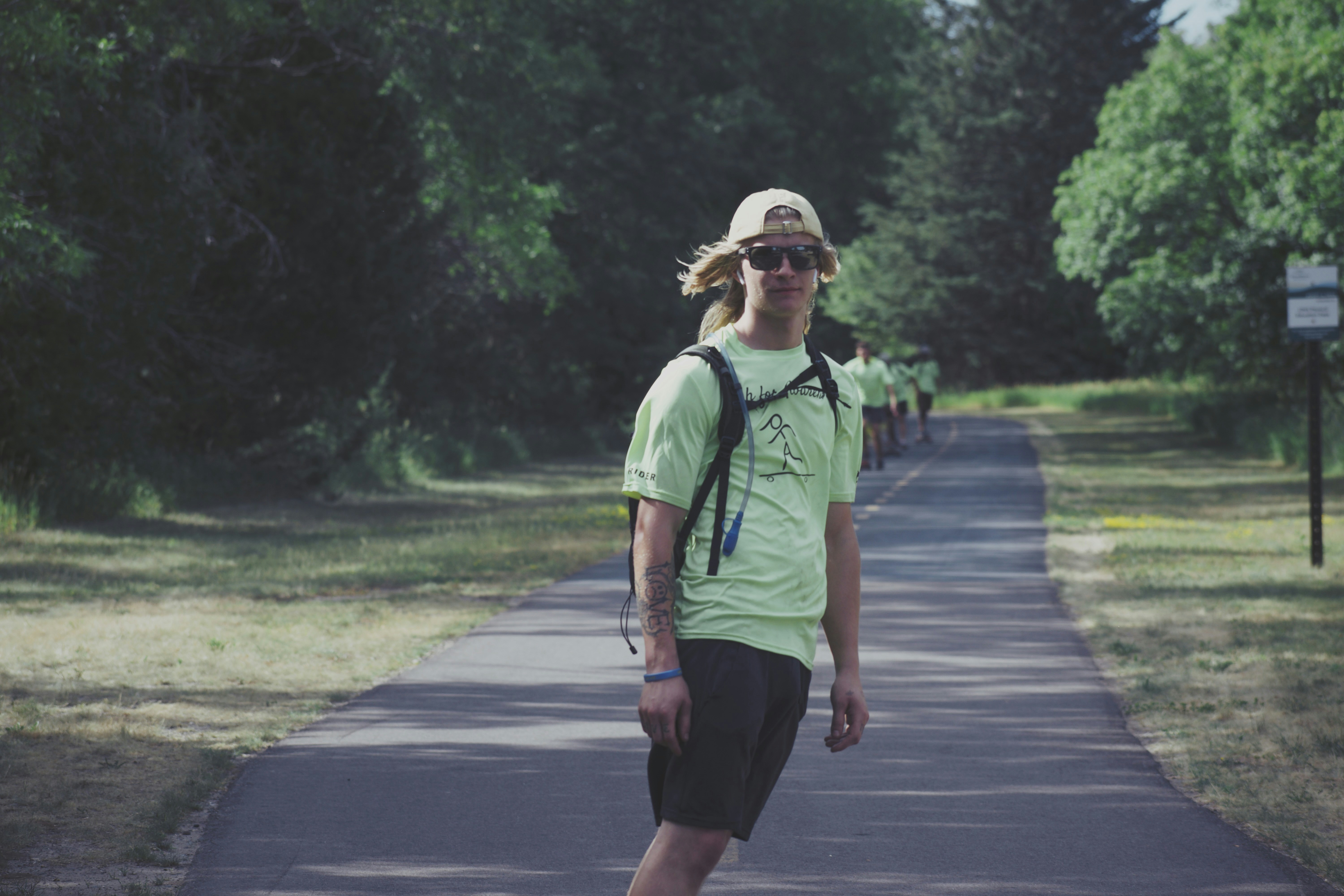 man in green crew neck t-shirt and black shorts walking on gray concrete road during