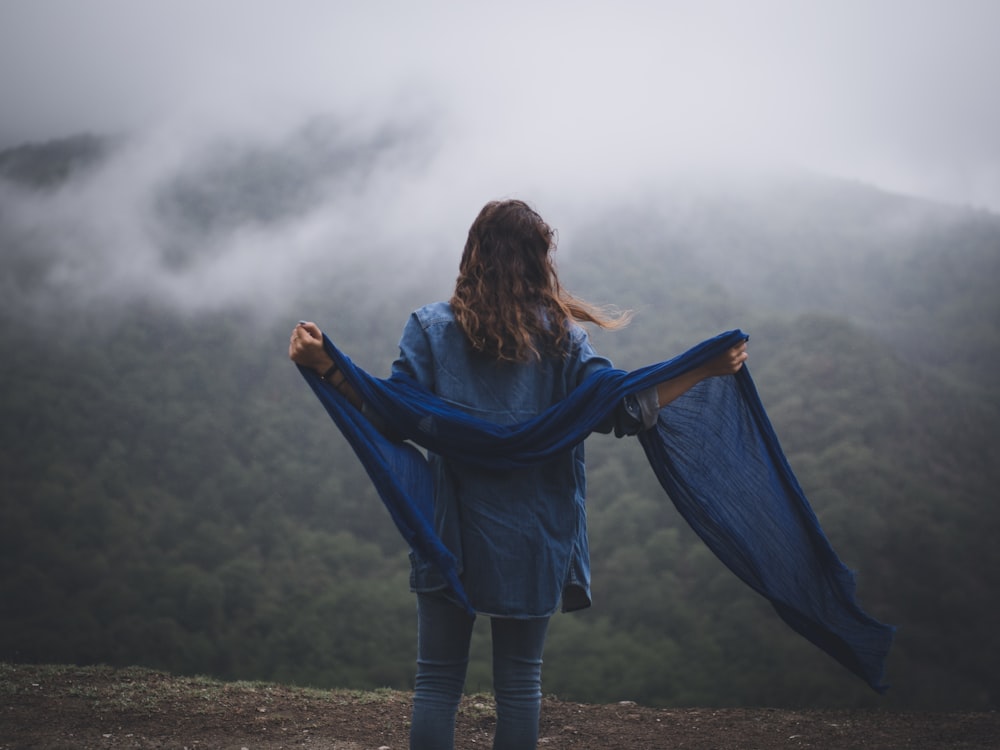 woman in blue long sleeve dress standing on green grass field under gray clouds during daytime