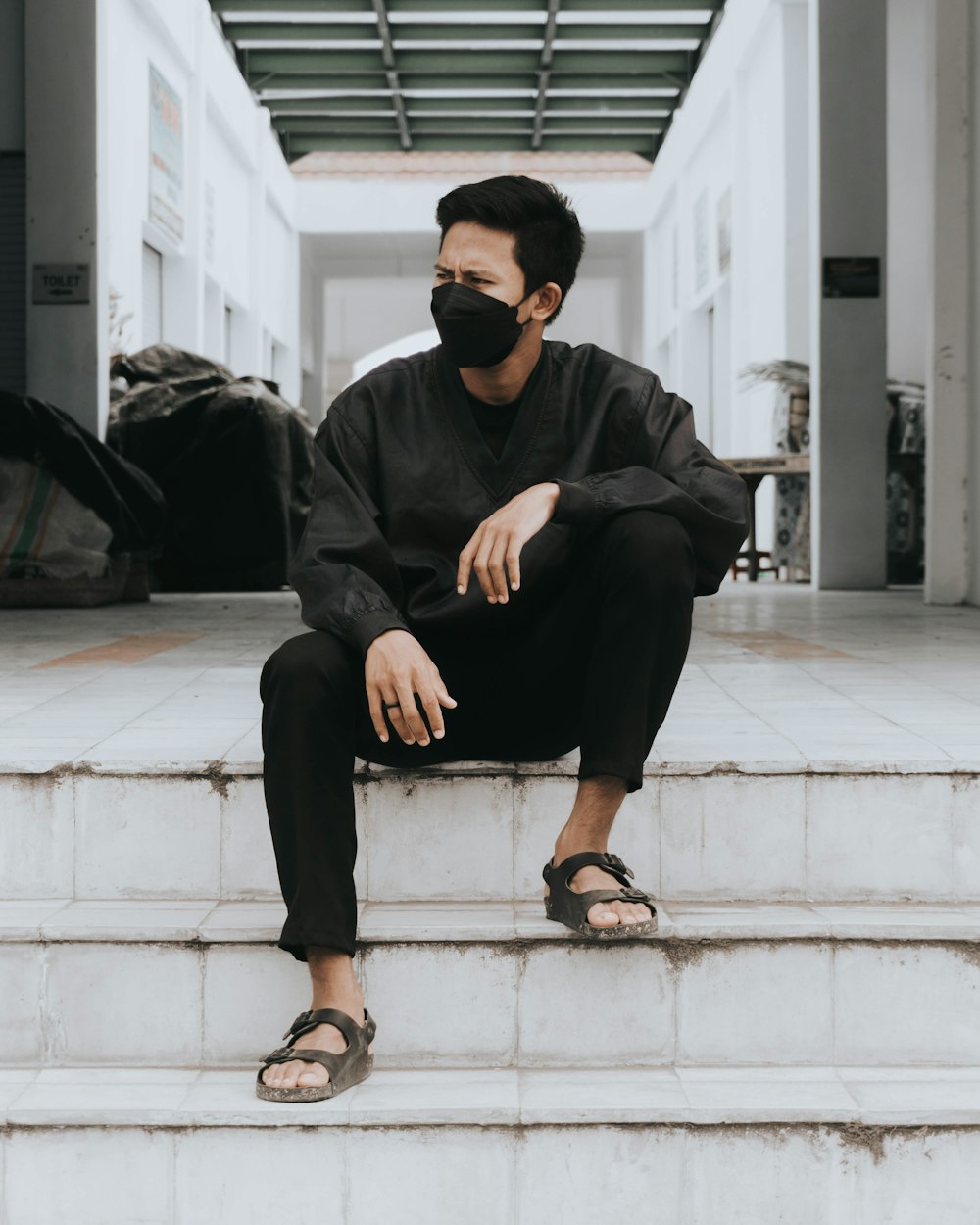 man in black jacket and black pants sitting on white concrete stairs