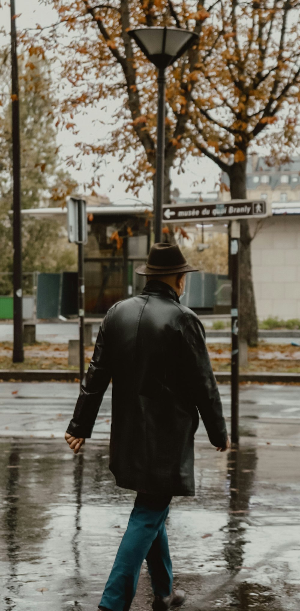 man in black leather jacket and black hat walking on sidewalk during daytime