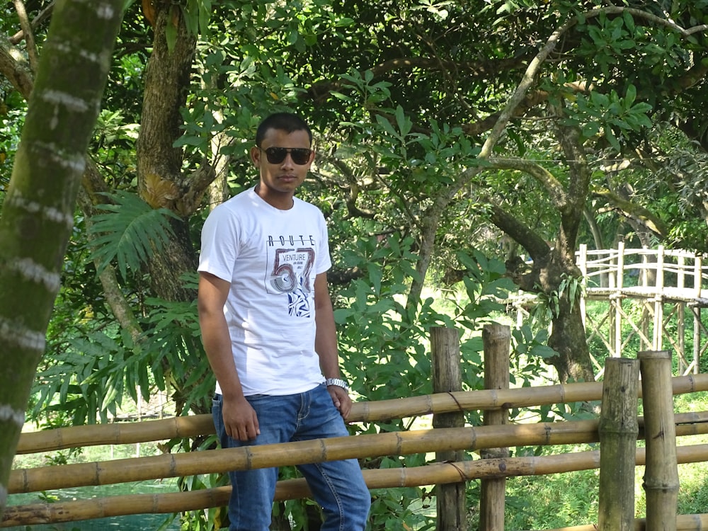 Hombre con camiseta blanca de cuello redondo de pie en un puente de madera marrón