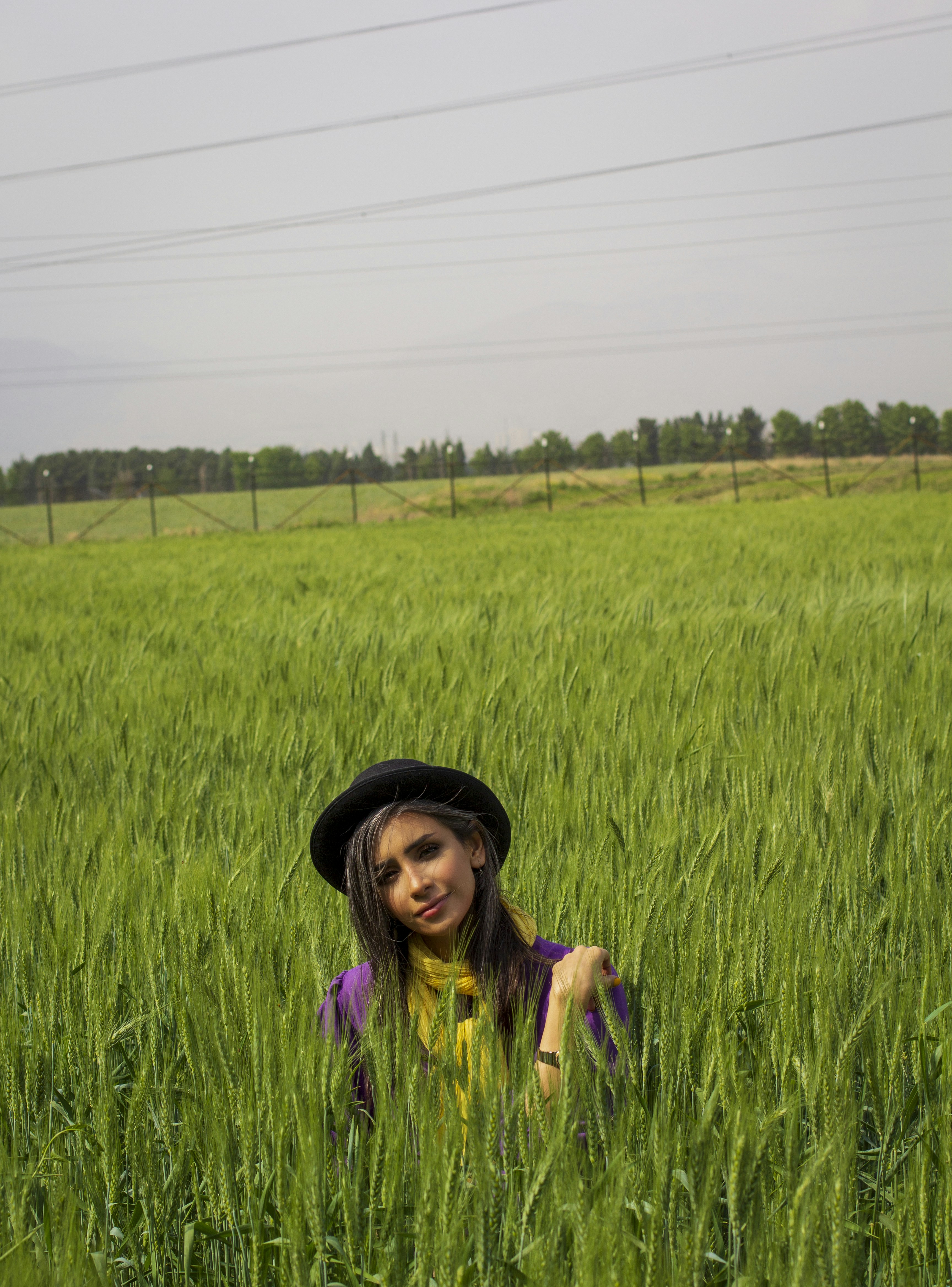 woman in purple shirt and black hat sitting on green grass field during daytime