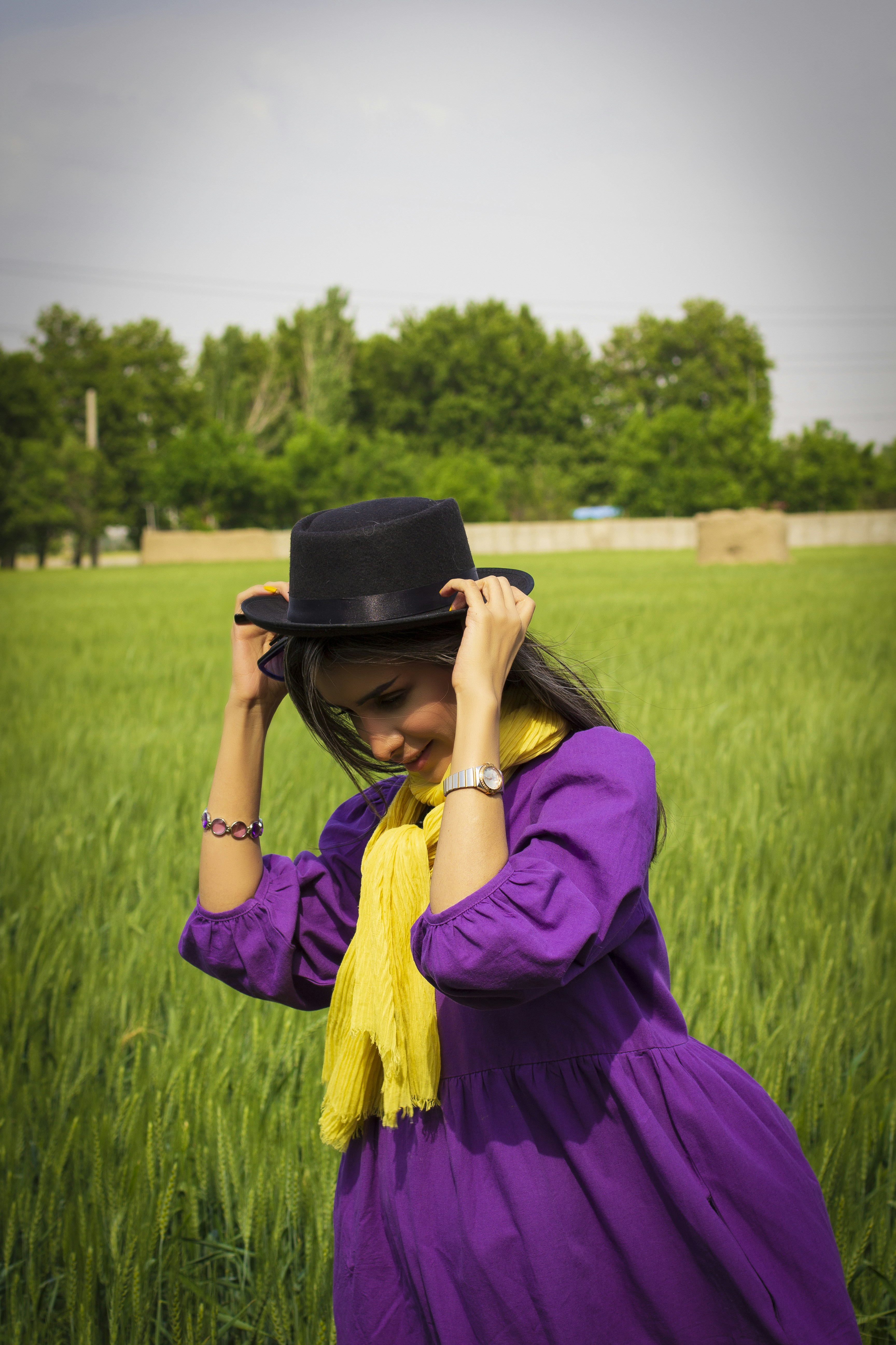 woman in purple long sleeve shirt and black hat sitting on green grass field during daytime